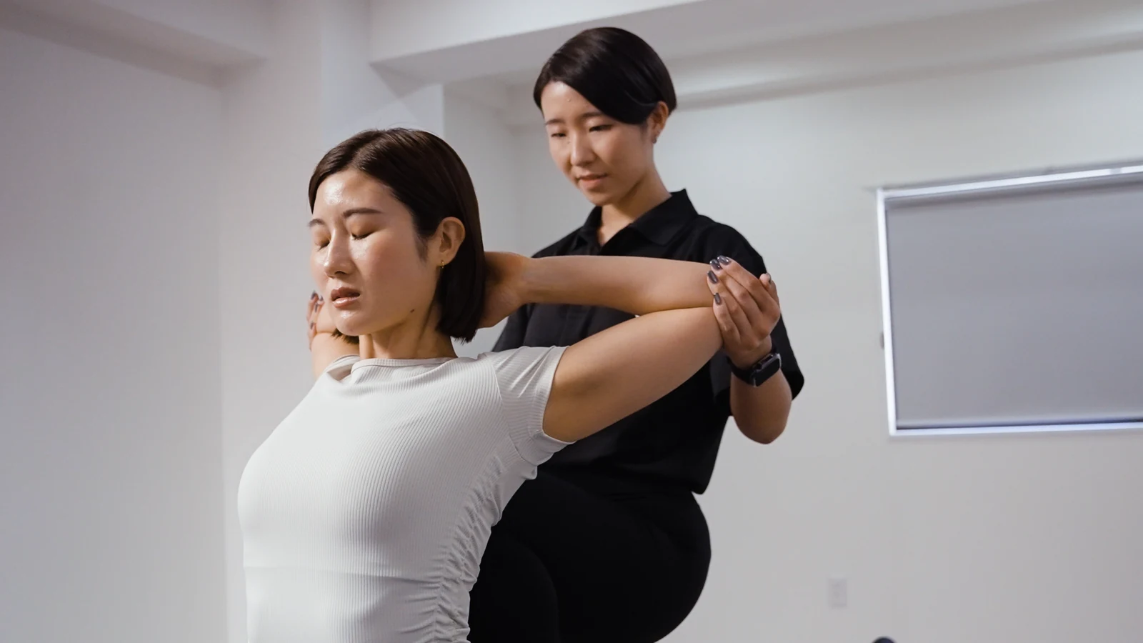 女性トレーナーが利用者の肩と胸をストレッチする様子